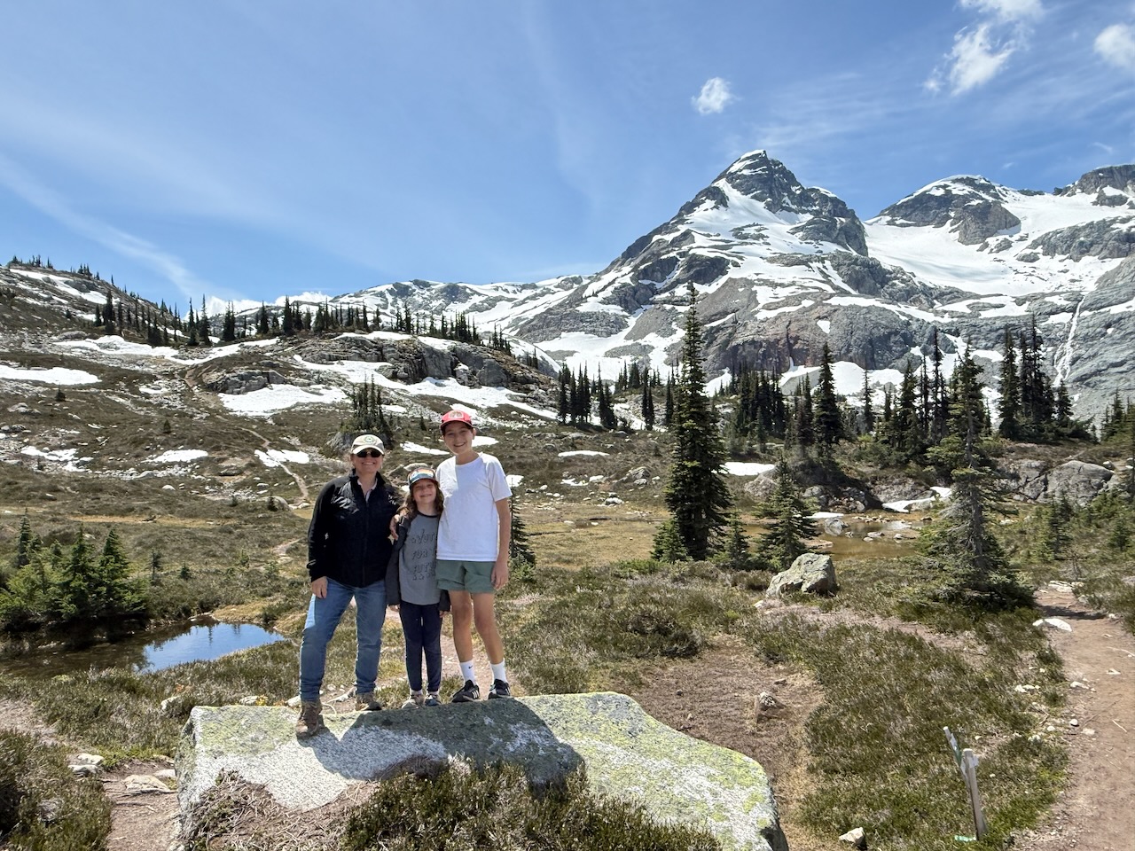 Meryl with her two kids on a rock below snowy peaks